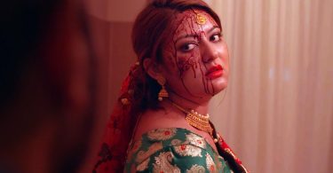 Barsha Raut in a bridal outfit, looking over her shoulder with blood marks on her face in a tense scene from the short film Missing Bride.